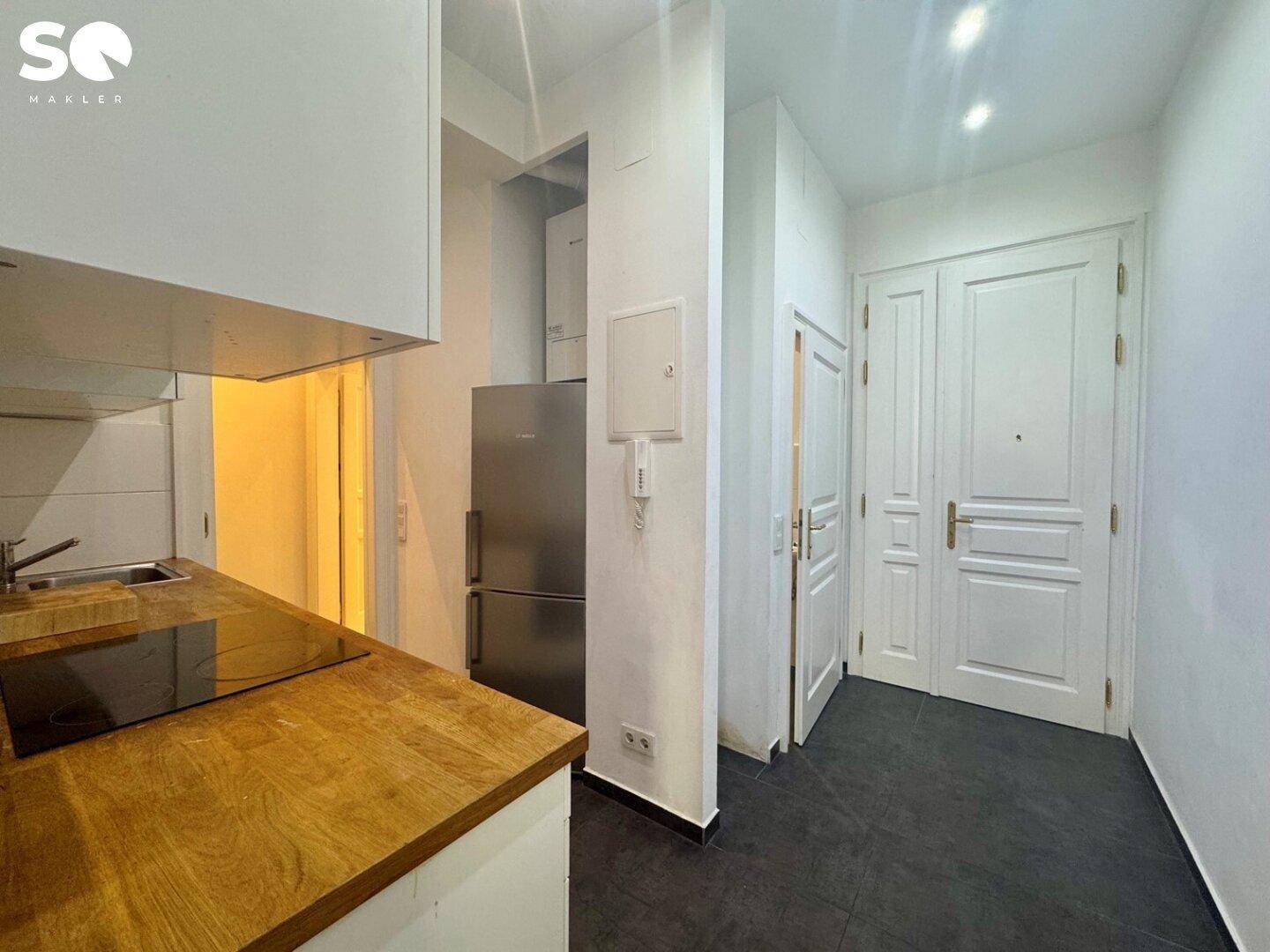 Kompakte Küchenzeile mit Holz-Arbeitsplatte, integriertem Kühlschrank und Induktionskochfeld.
