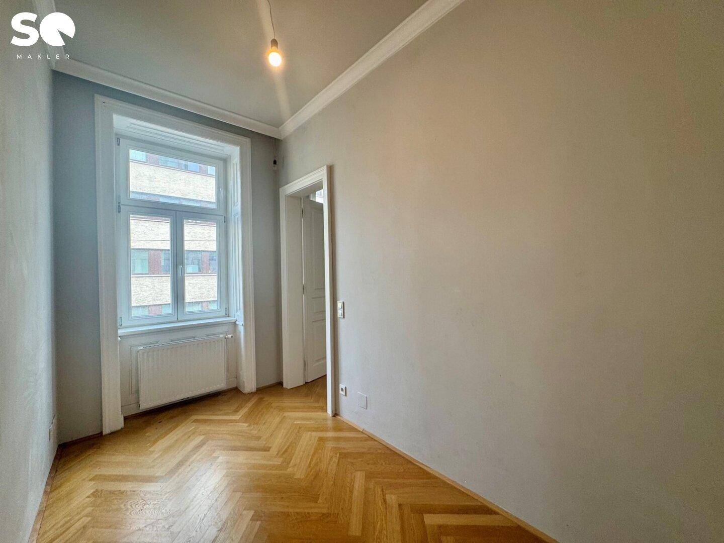 Kleineres Zimmer mit Fischgrätparkett und einem großen Fenster, ideal als Schlaf- oder Arbeitszimmer.
