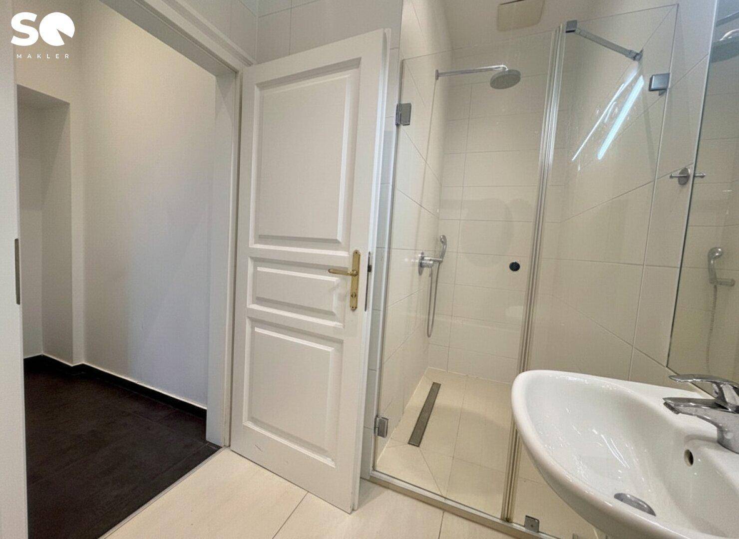 Modernes Badezimmer mit Duschkabine, Waschbecken und hellen Fliesen, funktional und sauber gestaltet.