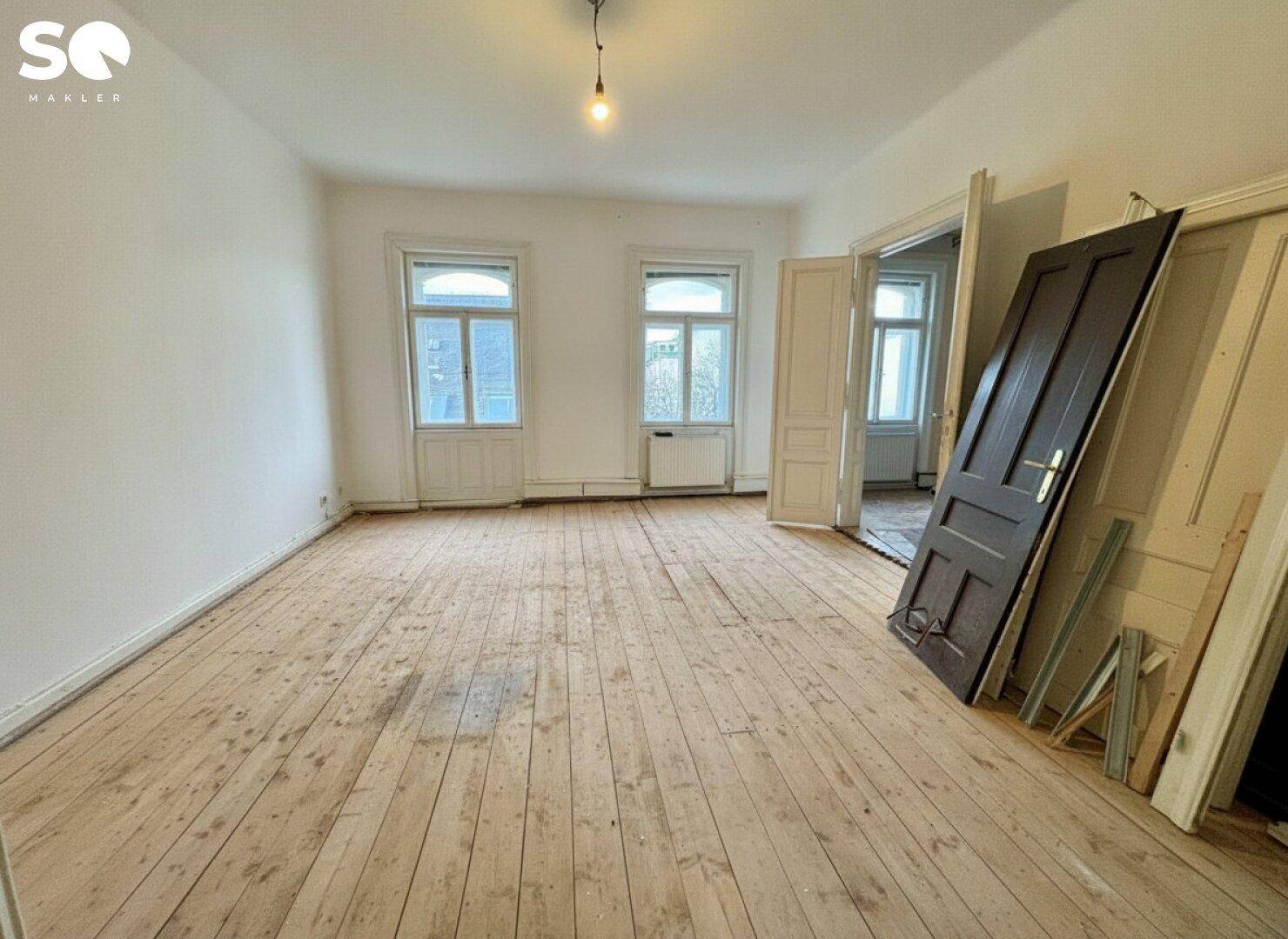 Heller Raum mit Dielenboden und hohen Fenstern, bereit für die Renovierung.