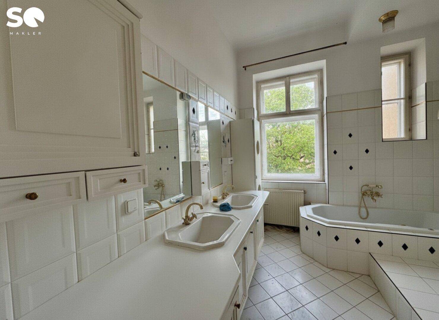 Badezimmer im 80er-Jahre-Stil mit Doppelwaschbecken, Badewanne und Fenster.