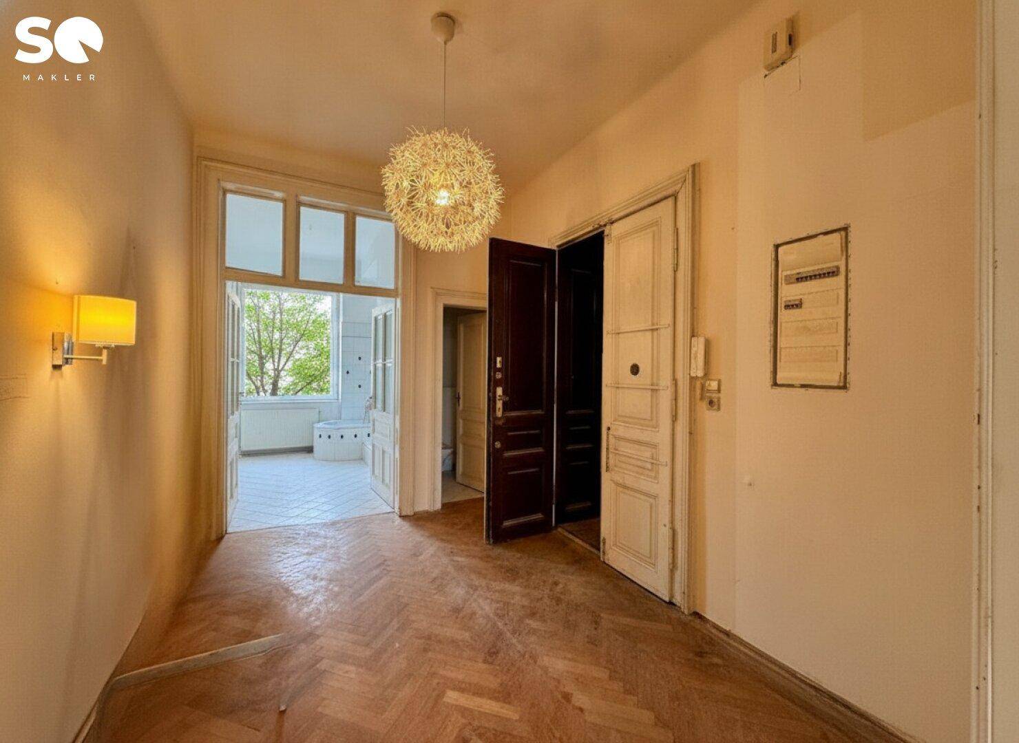 Eingangsbereich mit Fischgrätparkett und Zugang zu einem hellen Balkon.
