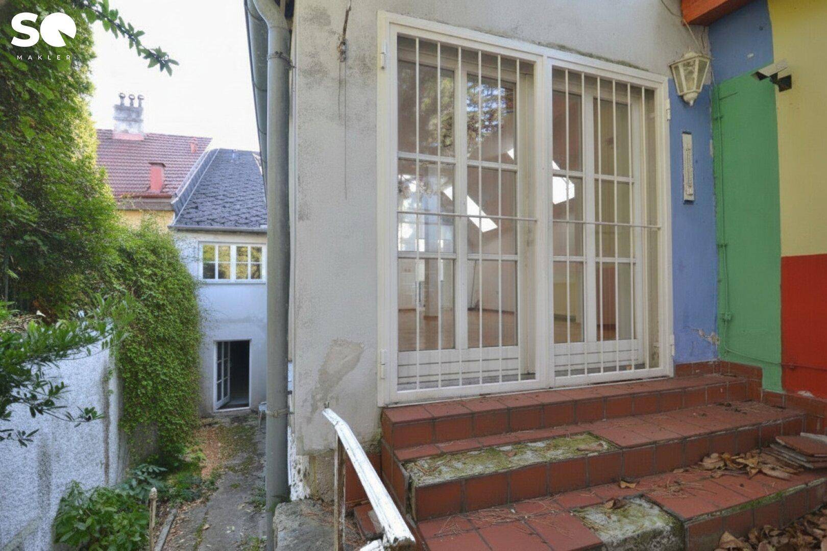 Eingangsbereich eines Gebäudes mit großer Glasschiebetür und Treppe.