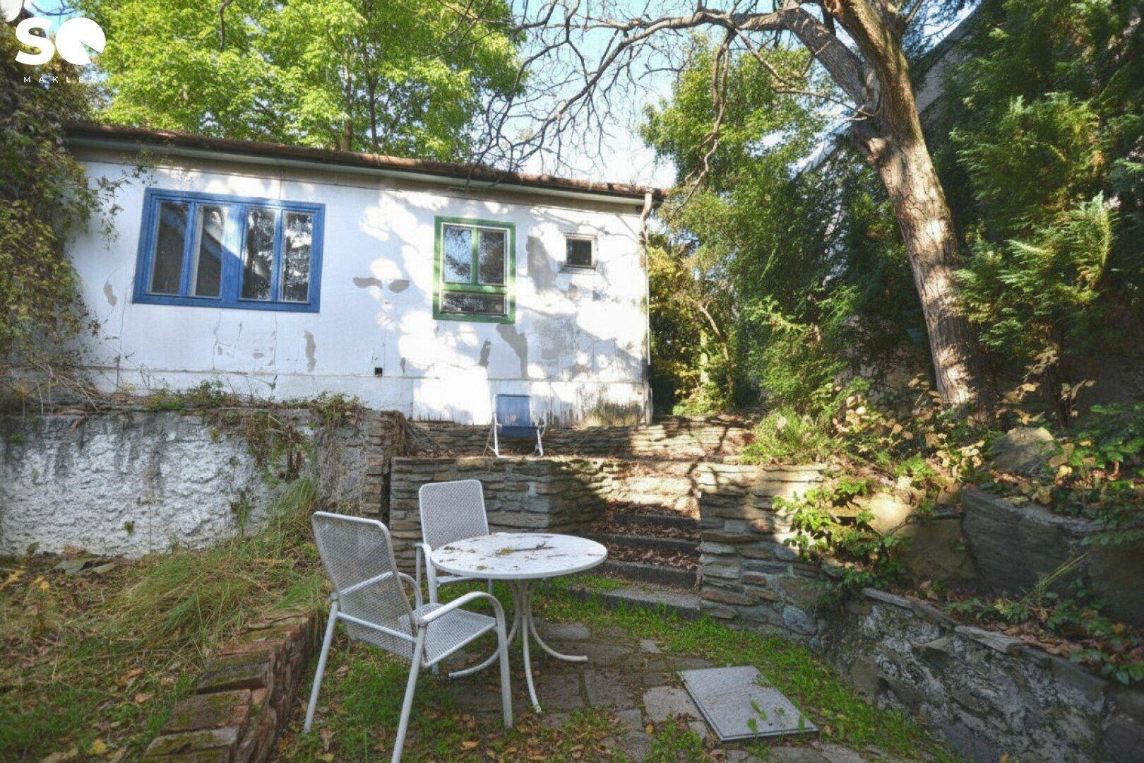 Gemütlicher Außenbereich mit Steinterrasse und Gartenmöbeln vor einem älteren Gebäude.