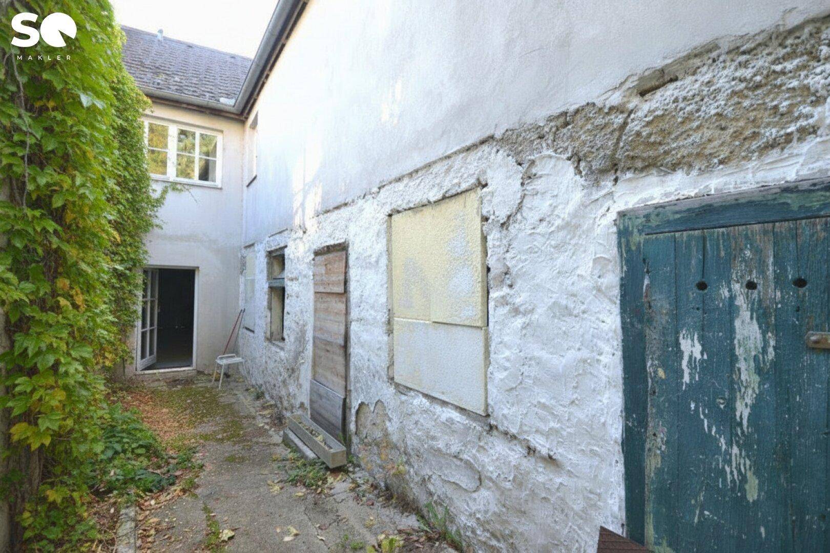 Alte Gebäudefassade mit Efeu bewachsen, zugenagelten Fenstern und einer verwitterten Holztür.