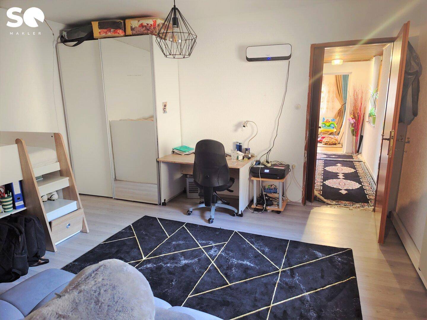 Schlafzimmer mit Schreibtisch, Kleiderschrank und modernem Teppich.