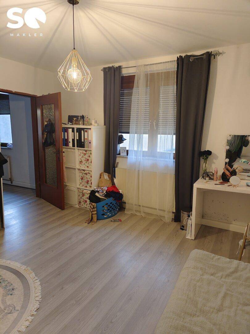 Helles Schlafzimmer mit Fenster, Vorhängen und Schminktisch.