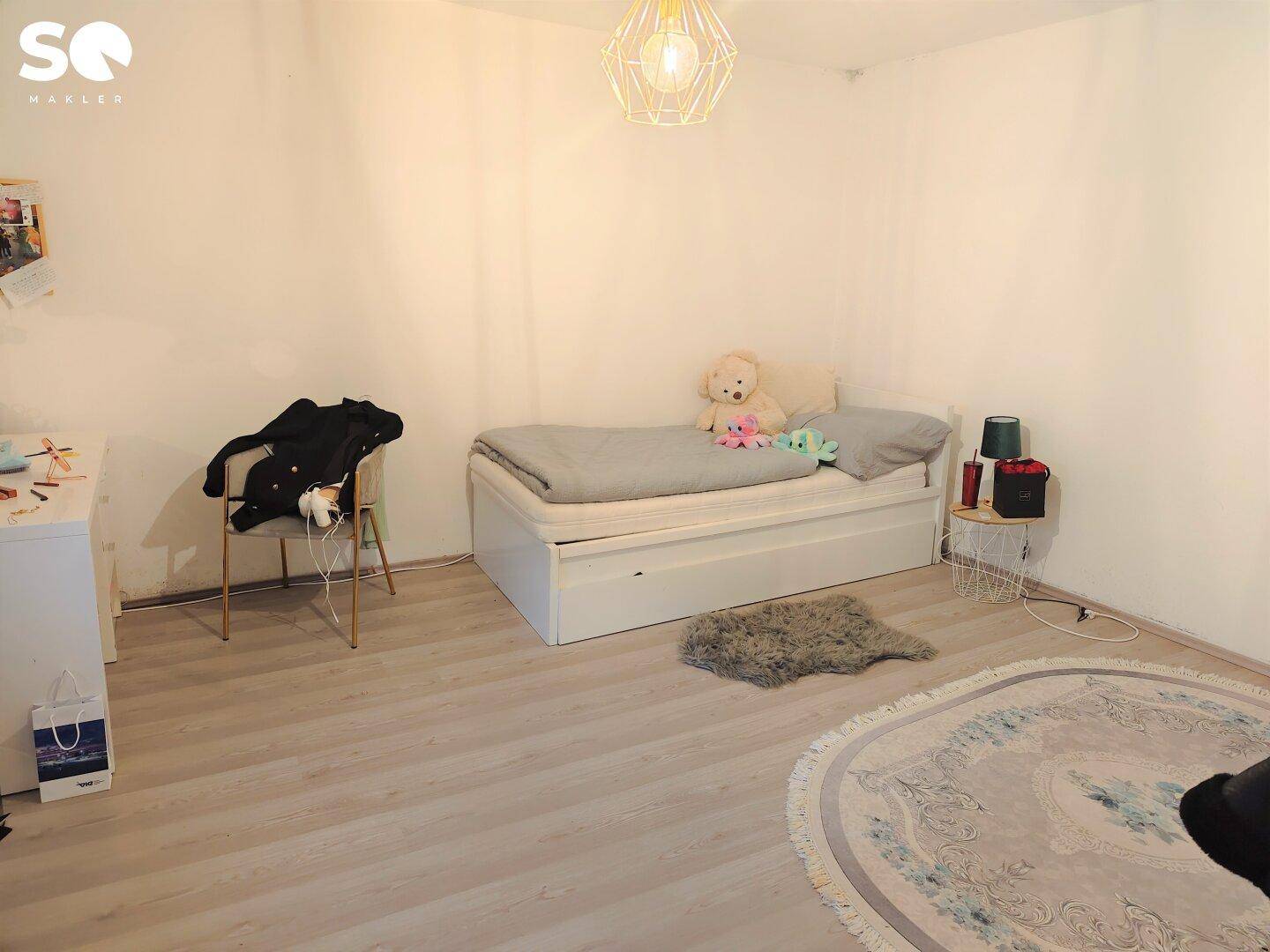 Schlafzimmer mit Einzelbett, hellem Laminatboden und rundem Teppich.
