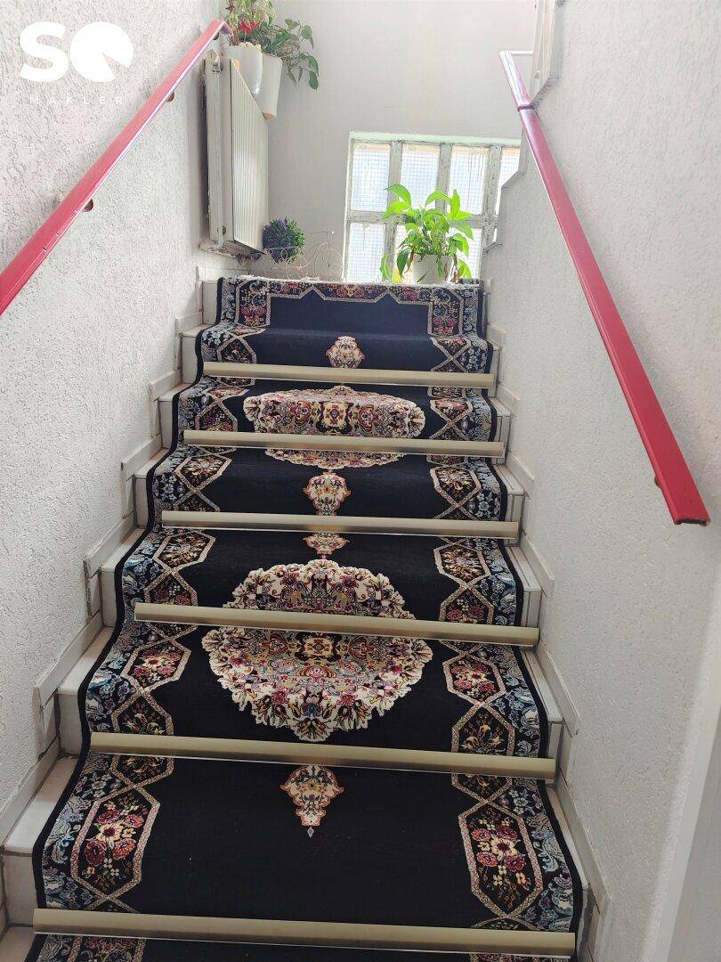 Treppenhaus mit gemustertem Teppichläufer und roten Handläufen.