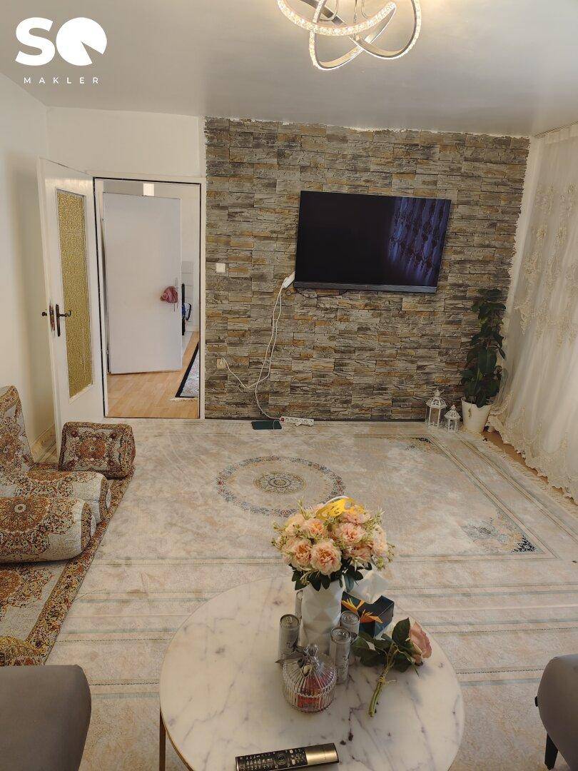 Wohnzimmer mit dekorativer Steinwand, montiertem Fernseher und gemustertem Teppich.