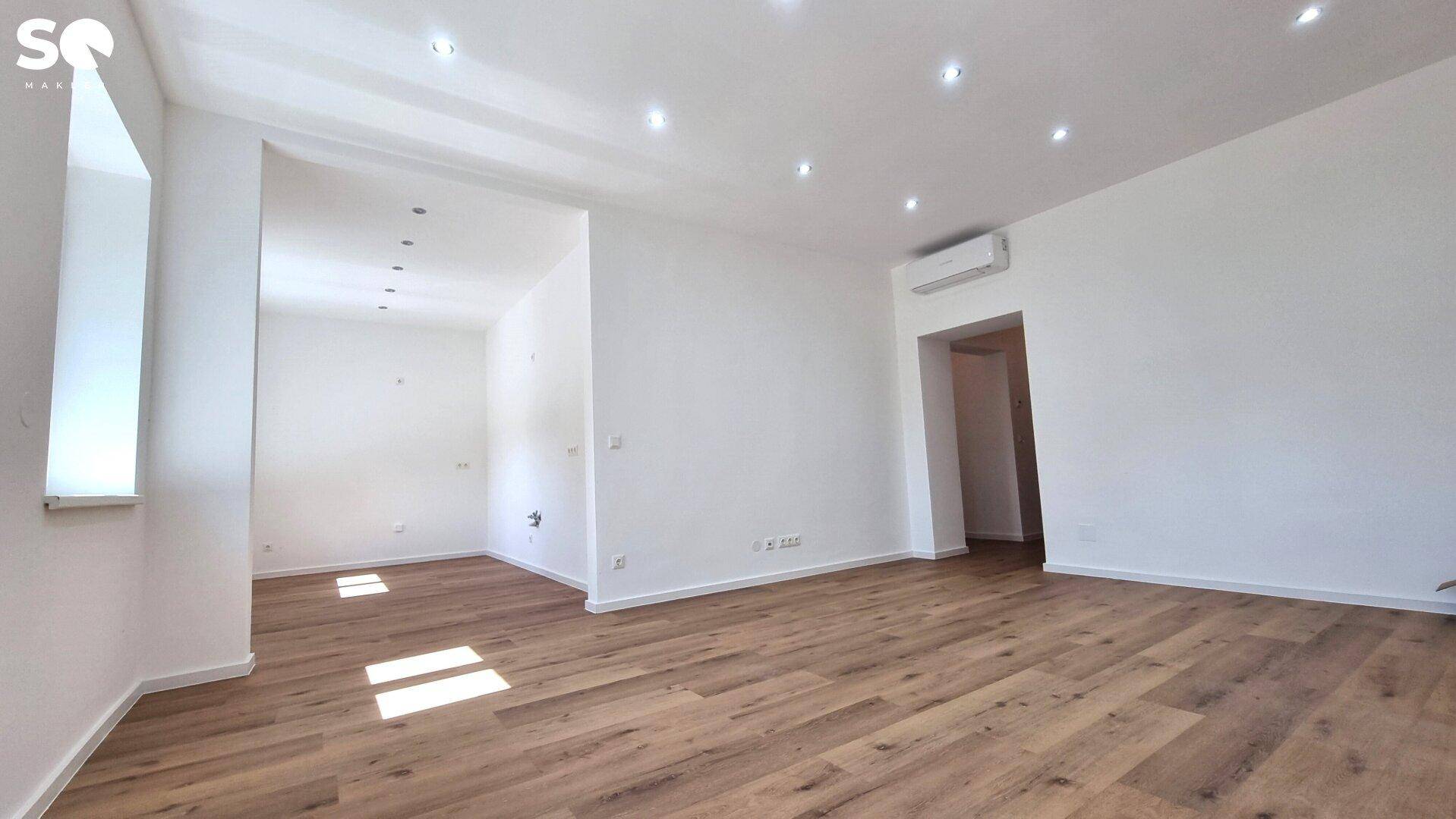 Heller, leerer Wohnraum mit modernem Laminatboden und integrierter Deckenbeleuchtung.