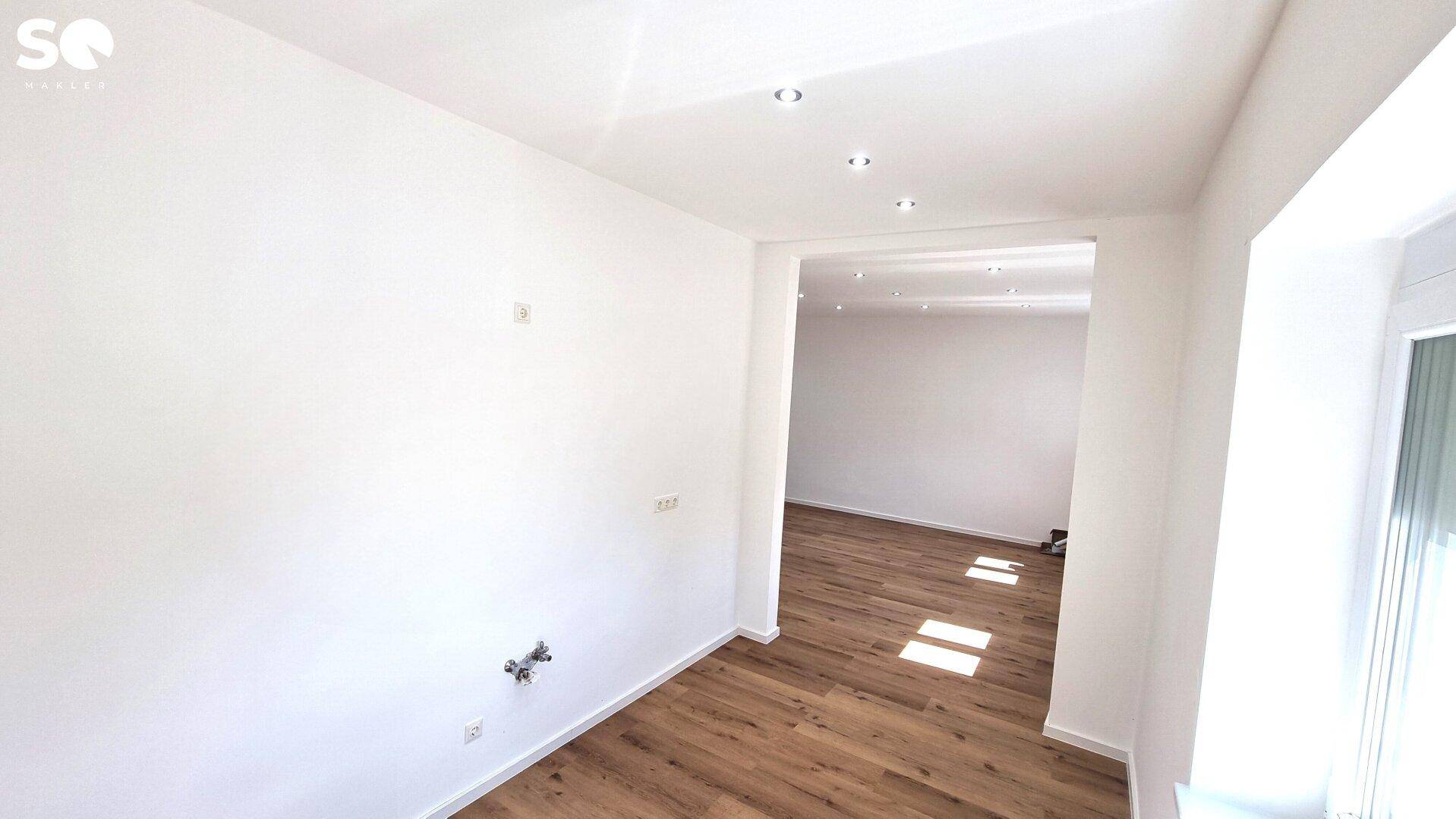 Heller Raum mit Laminatboden und Blick in einen weiteren Bereich mit Deckenstrahlern.