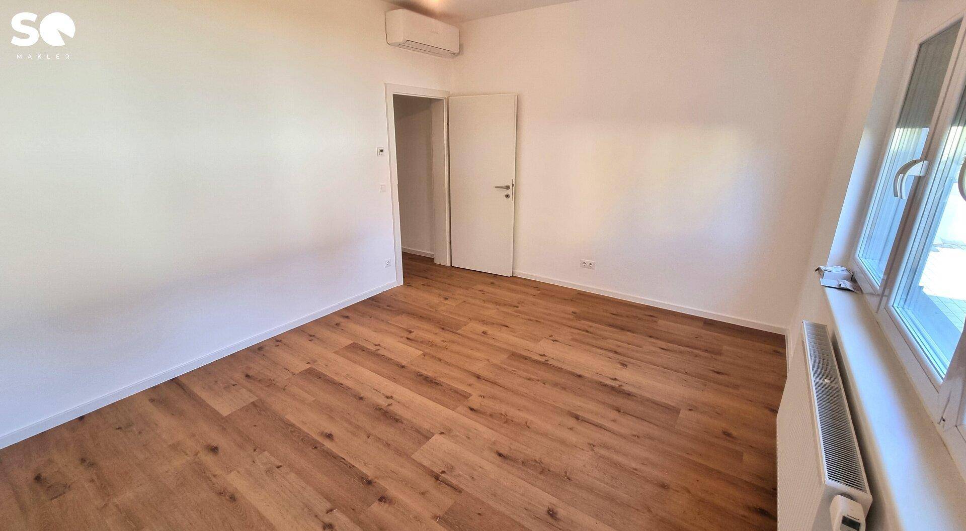 Leeres Schlafzimmer mit Laminatboden, Heizkörper und Fenster mit Rollläden.