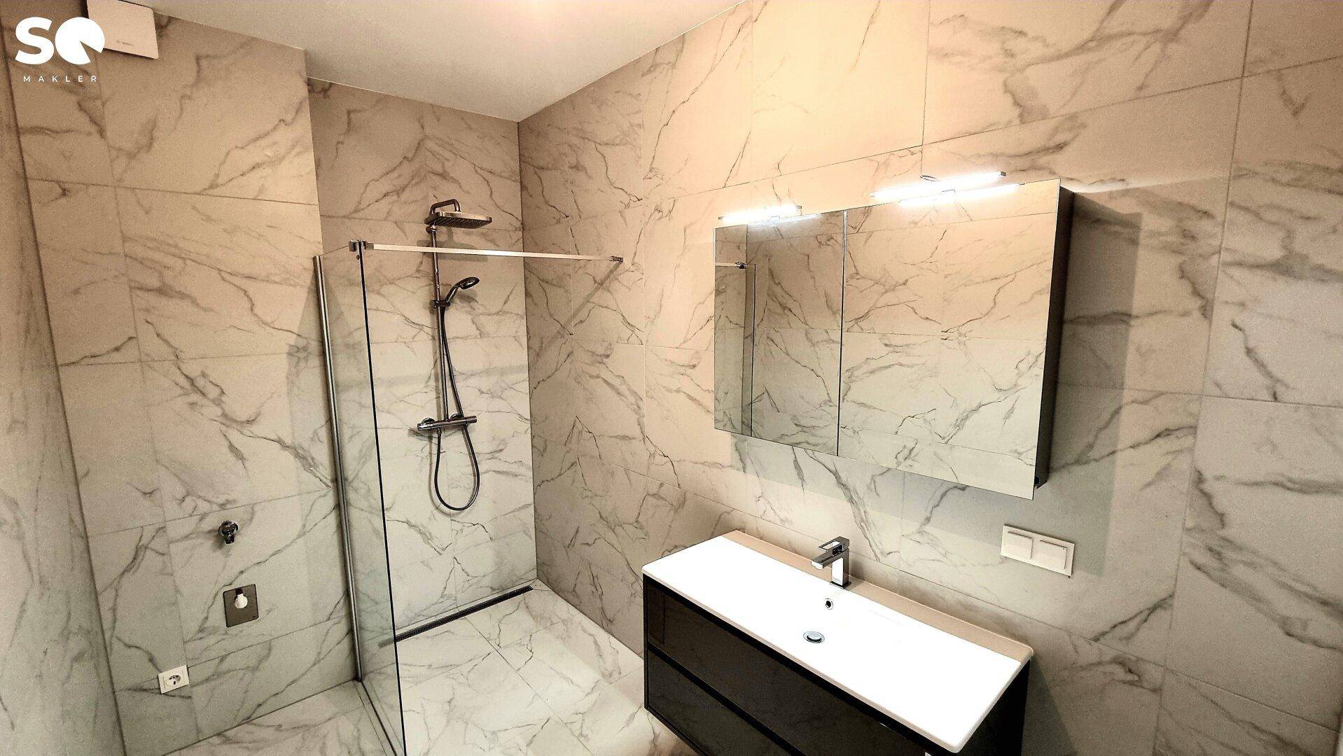 Modernes Badezimmer mit Marmorfliesen, ebenerdiger Dusche und Waschtisch mit Spiegelschrank.