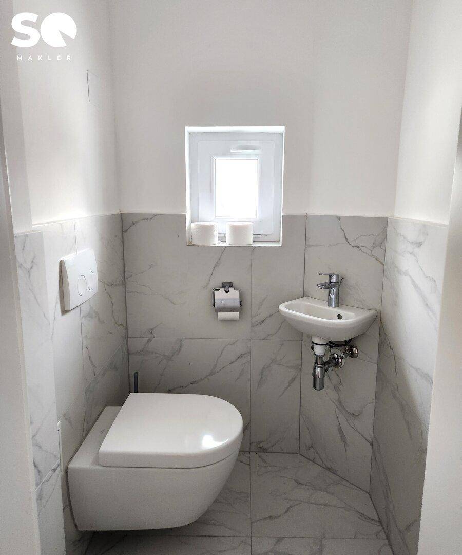 Kleines Gäste-WC mit Wand-WC, Handwaschbecken und Fenster.