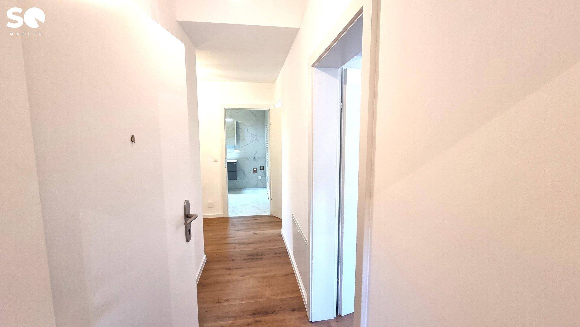 Heller Flur mit Laminatboden und Blick auf ein Badezimmer am Ende des Ganges.