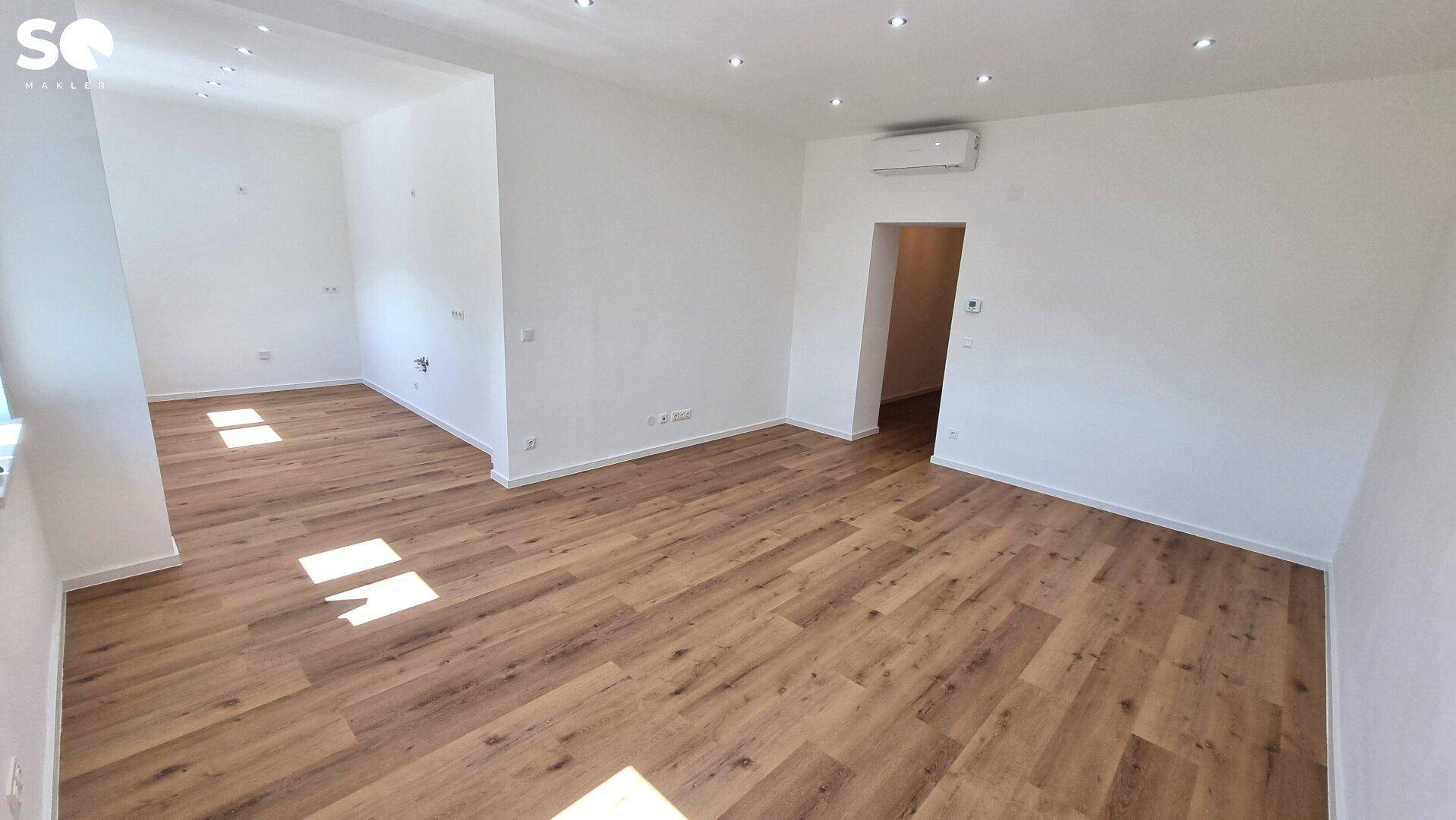 Heller, leerer Wohnraum mit modernem Laminatboden und integrierter Deckenbeleuchtung.
