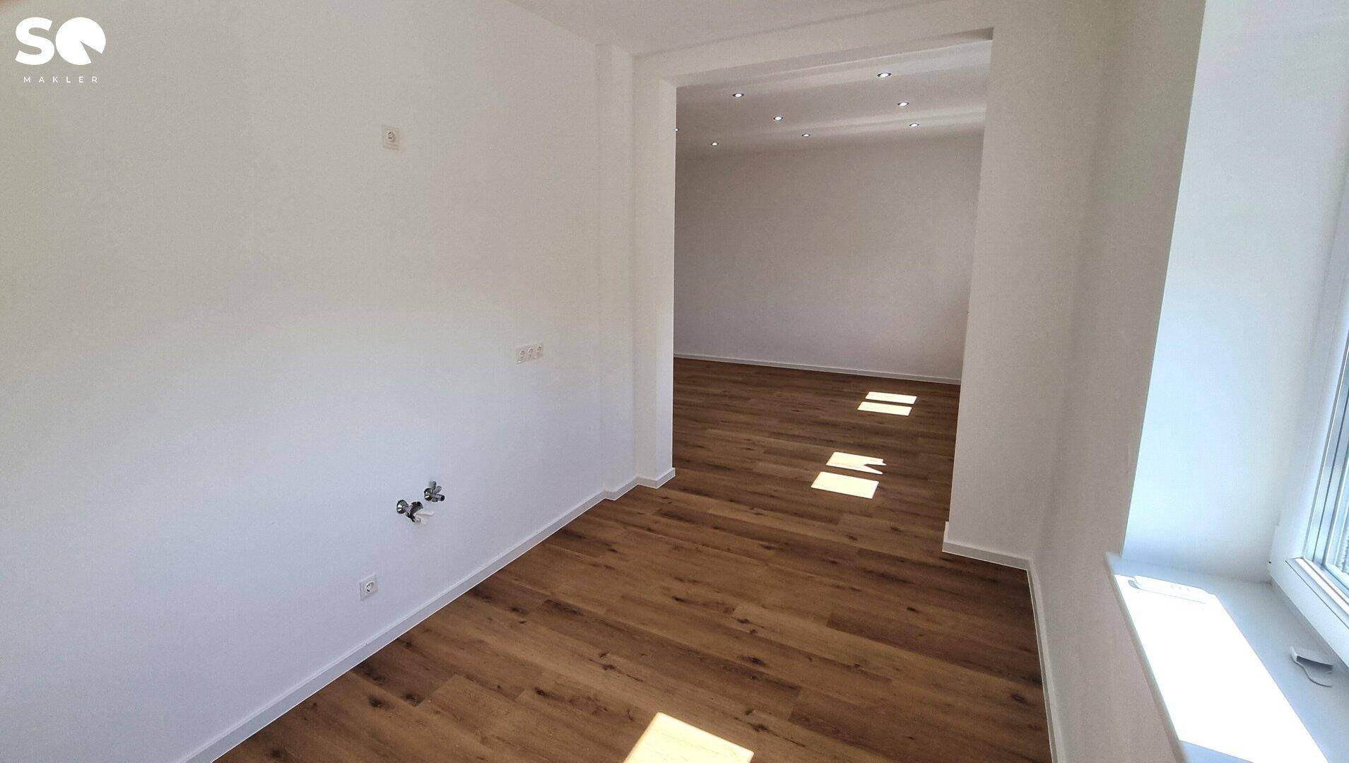 Heller Raum mit Laminatboden und Blick in einen weiteren Bereich mit Deckenstrahlern.