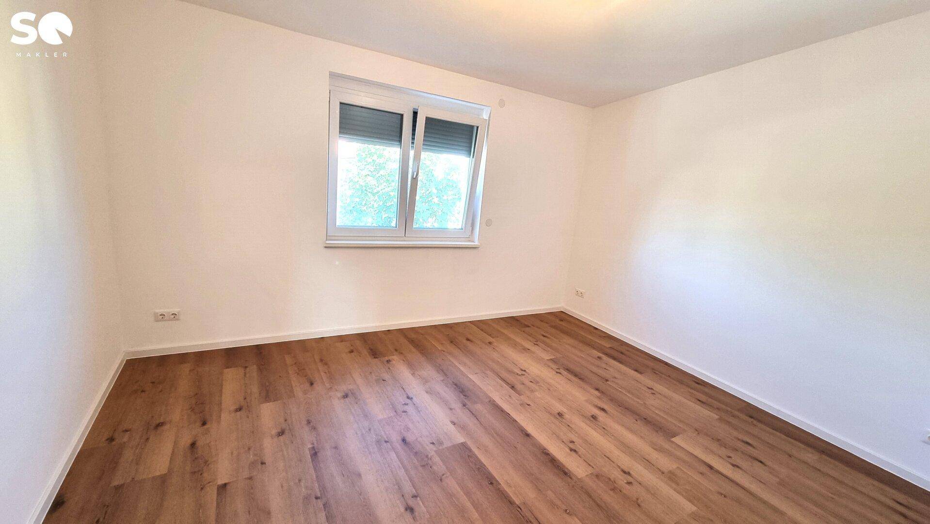 Helles Schlafzimmer mit Laminatboden, großem Fenster und Heizkörper unter dem Fenster.
