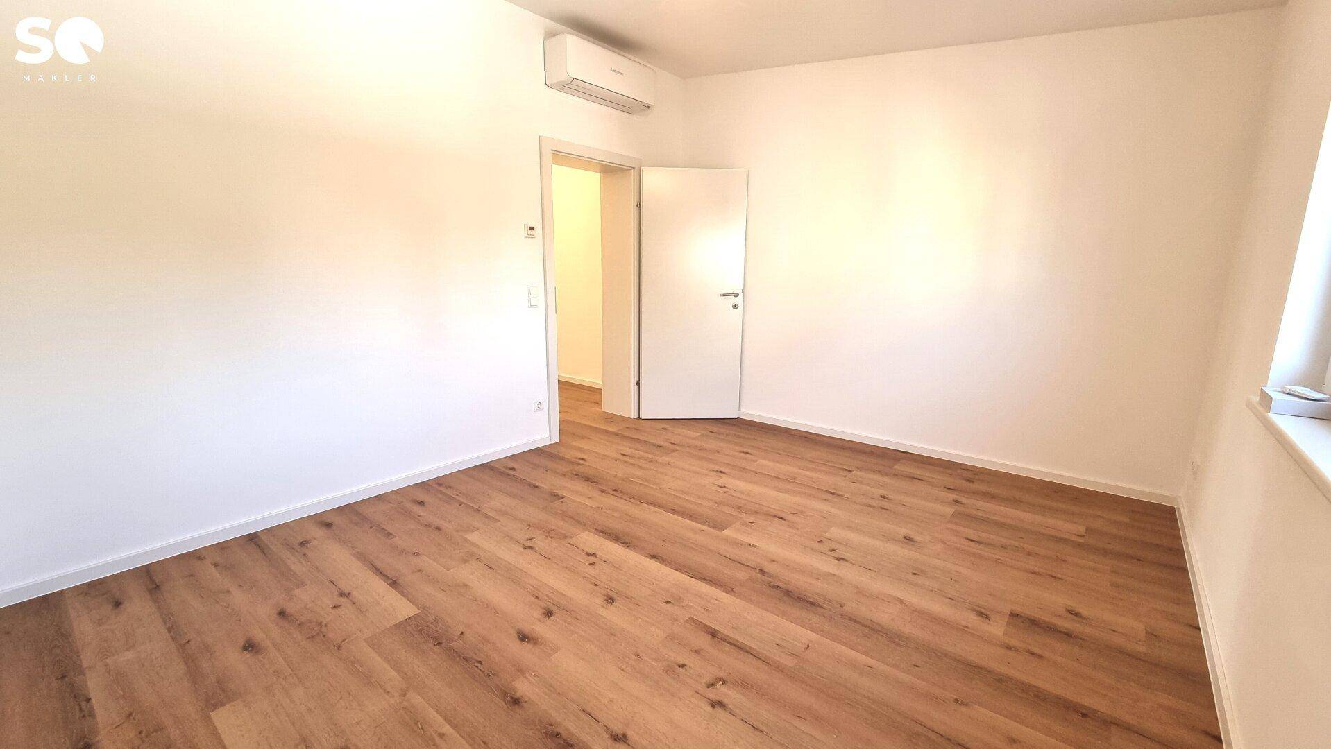 Leeres Schlafzimmer mit Laminatboden, Heizkörper und Fenster mit Rollläden.