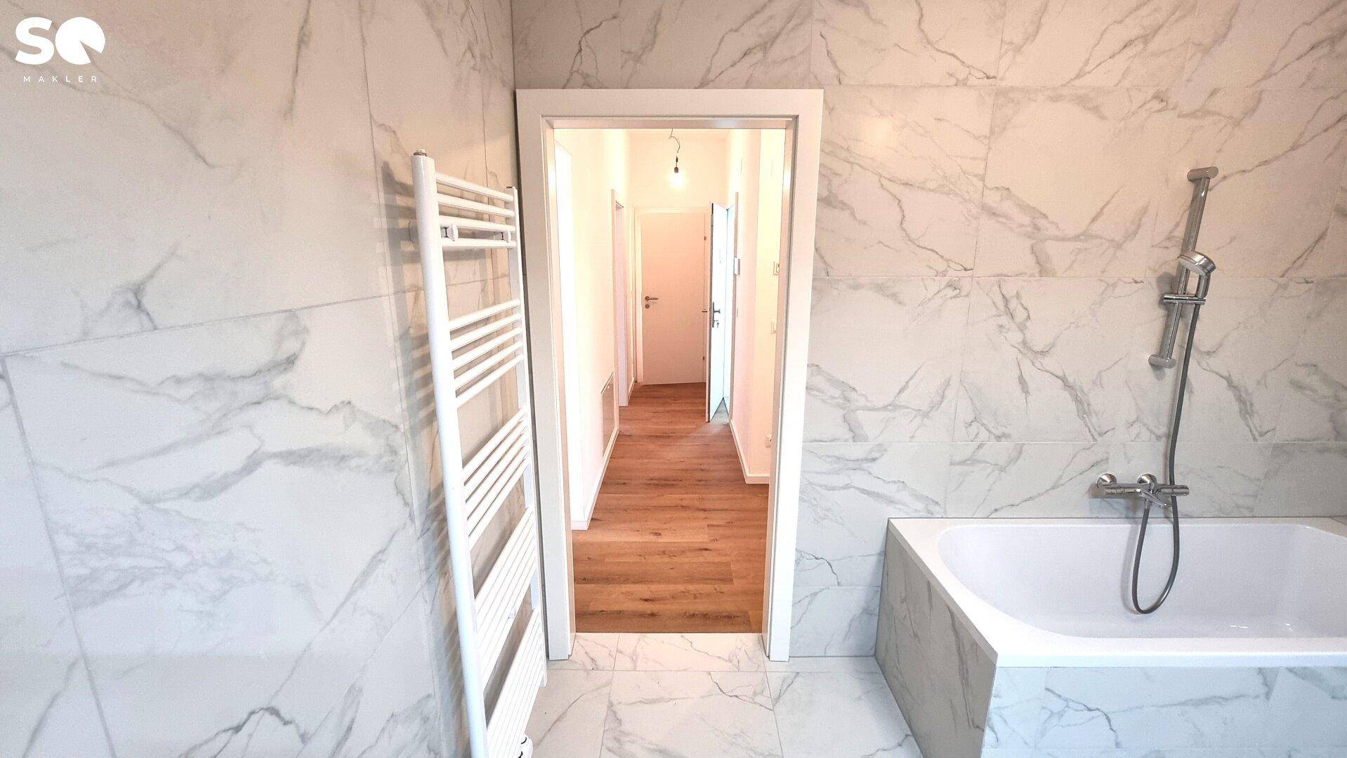 Modernes Badezimmer mit Badewanne und beheiztem Handtuchhalter, Blick in den Flur.