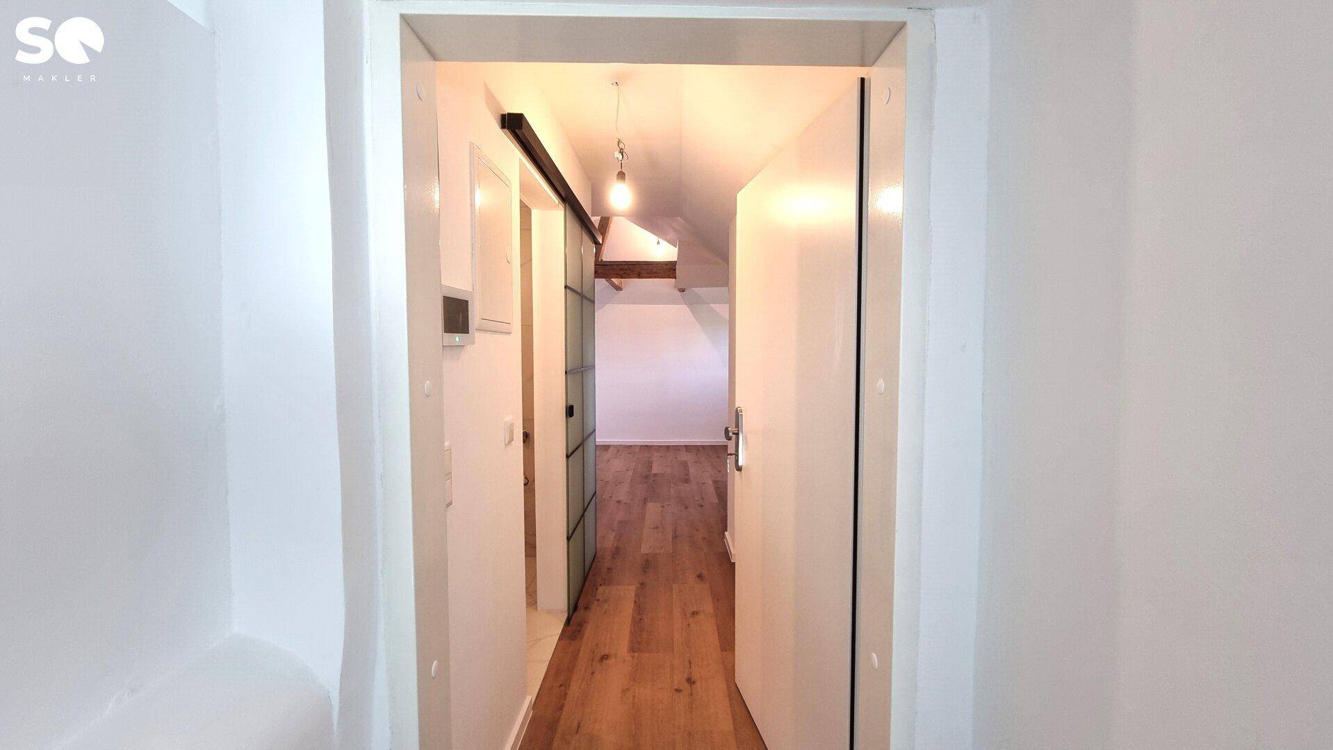 Heller Flur mit Holzboden und moderner Schiebetür, die den Blick in einen Raum mit Holzbalken freigibt.