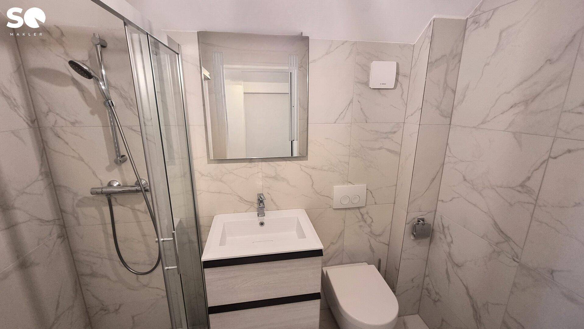 Funktionales Badezimmer mit Marmoroptik-Fliesen, Waschtisch, wandhängendem WC und Duschbereich.