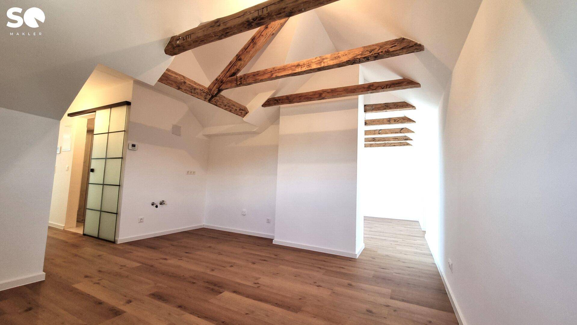 Heller Dachbodenraum mit rustikalen Holzbalken, Holzboden und moderner Schiebetür.