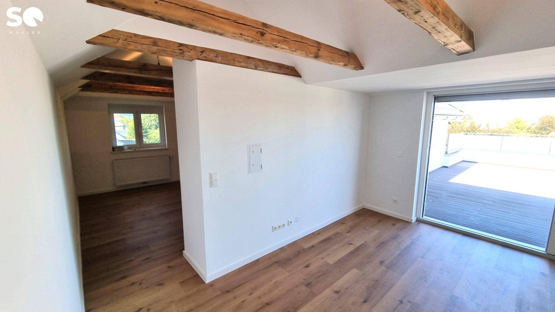 Dachbodenraum mit Holzboden, sichtbaren Balken und großem Schiebefenster mit Zugang zur Terrasse.