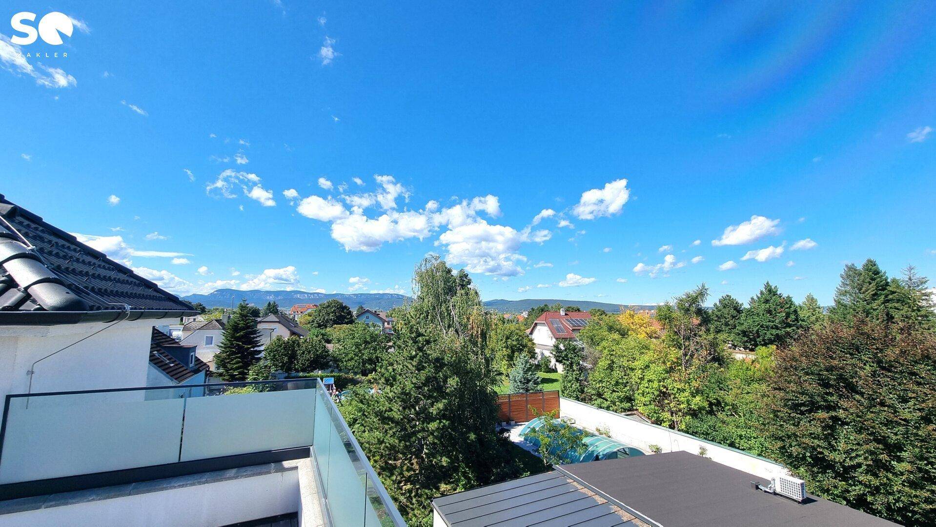Panoramablick von der Terrasse über eine grüne Wohngegend mit Häusern und Bergsilhouette.