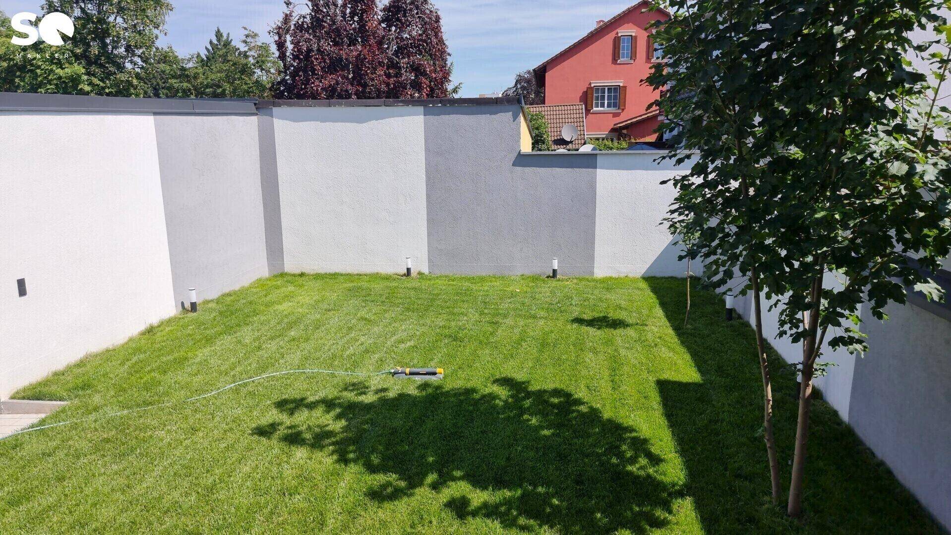 Gepflegte Rasenfläche im Garten, umgeben von einer modernen, zweifarbigen Mauer.