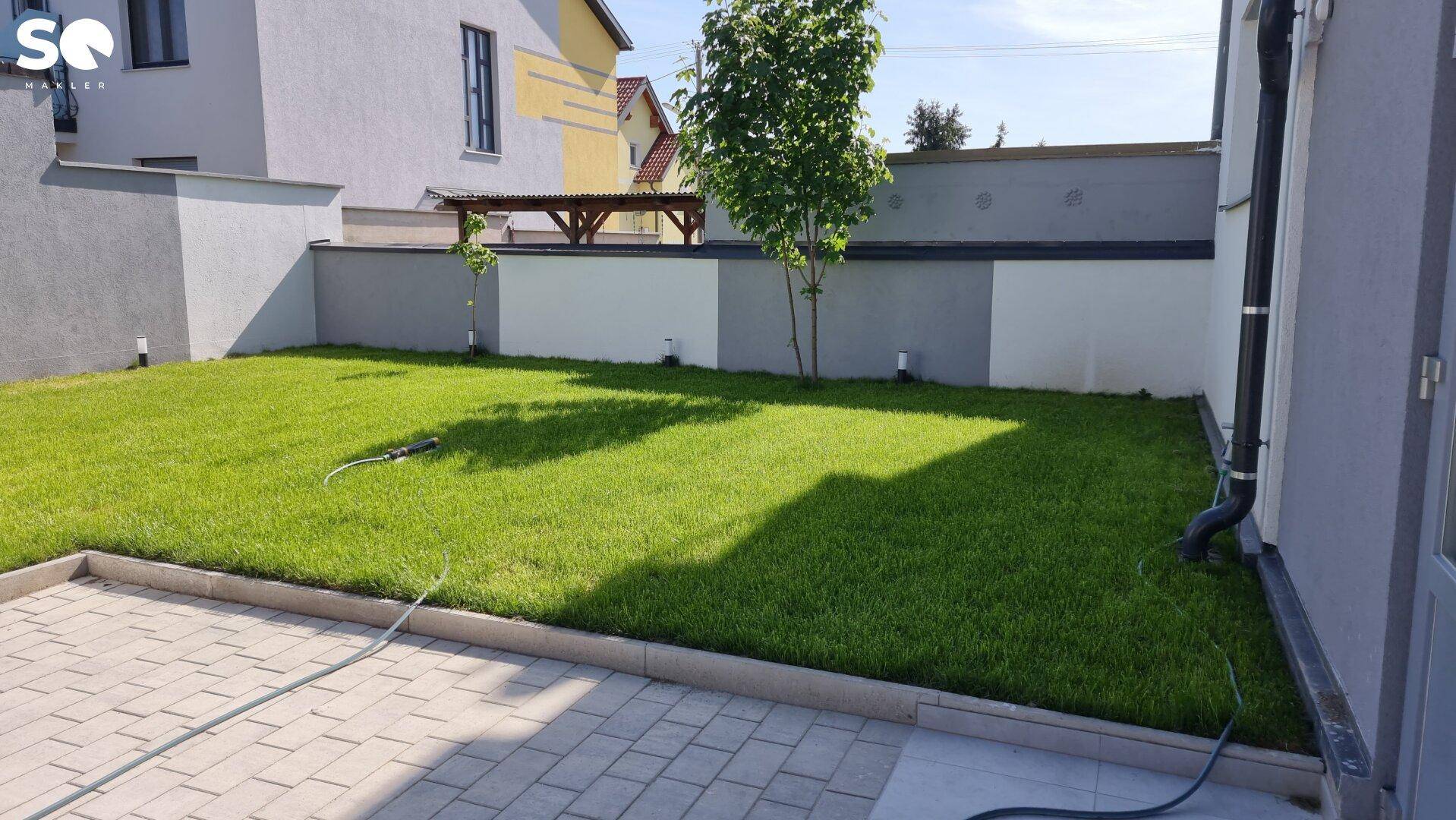 Kleine, gepflegte Rasenfläche neben einem gepflasterten Bereich, umgeben von einer modernen Mauer.