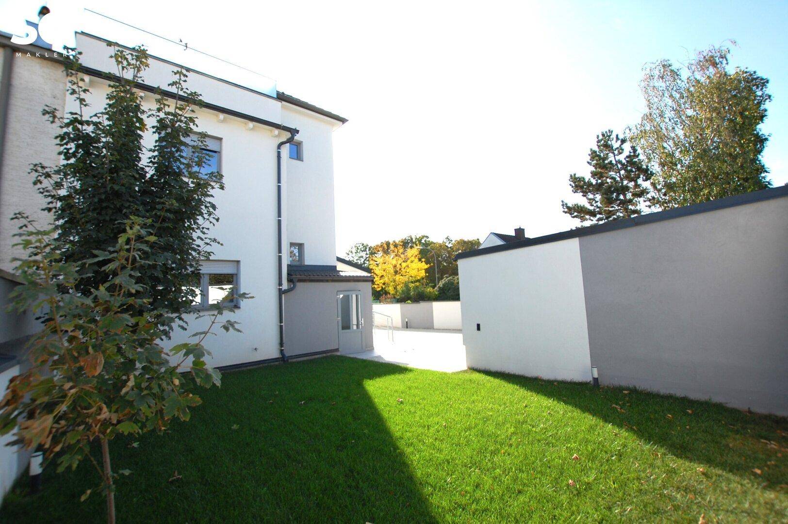 Seitenansicht eines modernen Hauses mit grüner Rasenfläche und gepflastertem Bereich im Hintergrund.