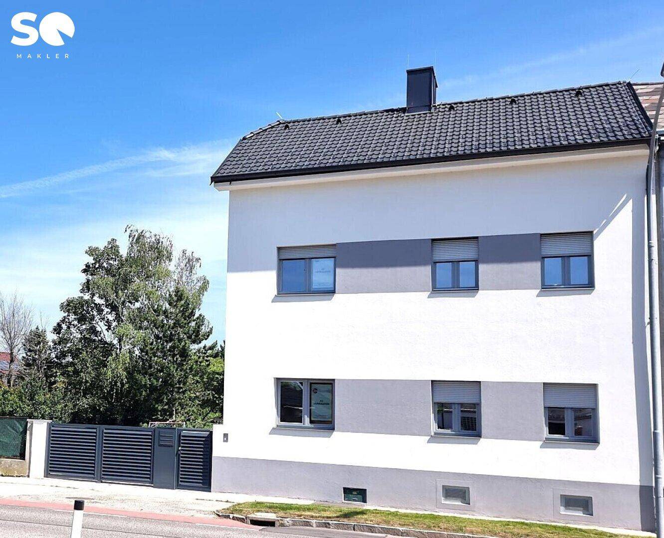 Moderne Hausfassade in Weiß und Grau mit Fenstern, Rollläden und Ziegeldach.