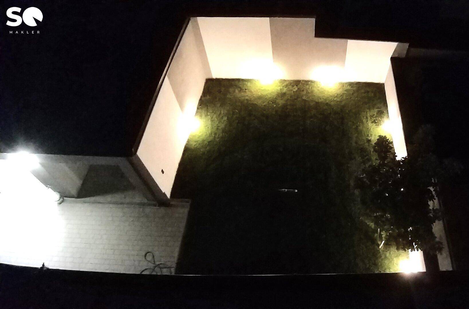 Gartenbereich und Gebäudeseite bei Nacht, effektvoll beleuchtet durch Bodenstrahler.