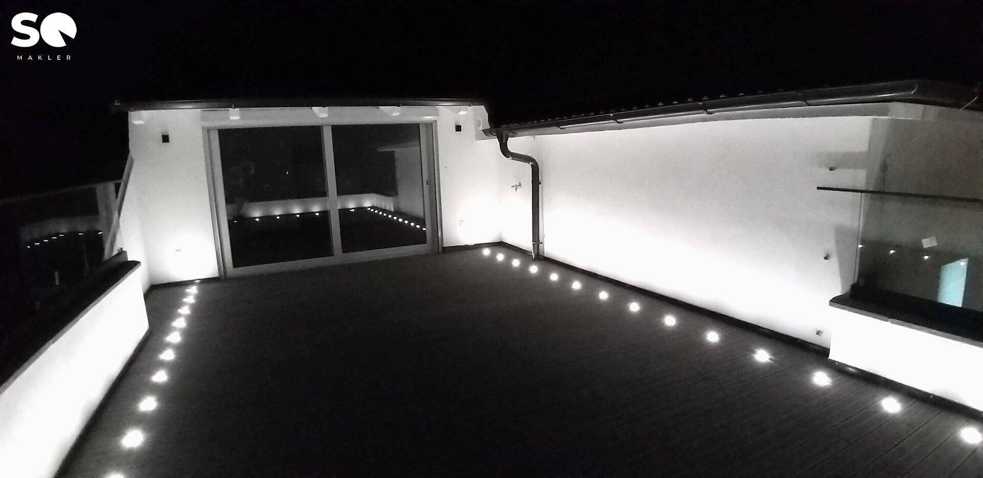 Beleuchtete Dachterrasse bei Nacht mit modernen Bodenleuchten und Zugang zu Innenräumen.