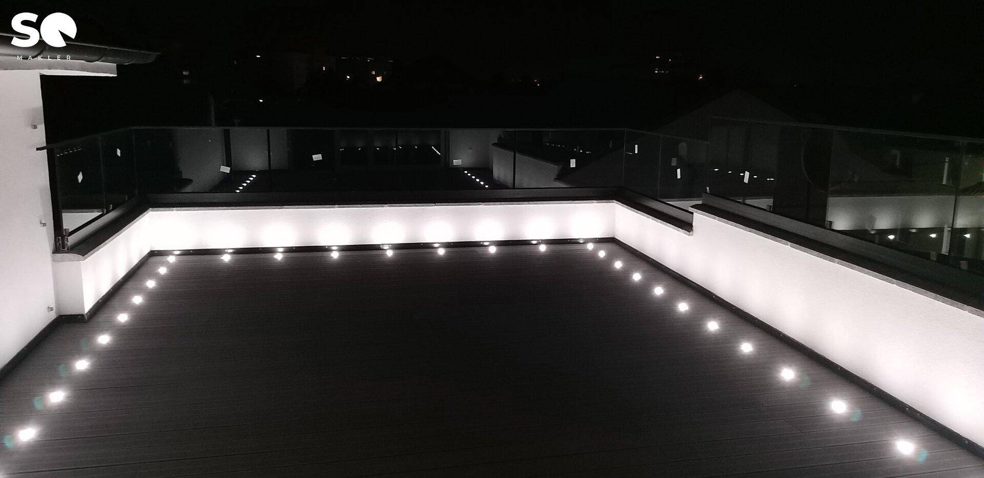 Weitläufige Dachterrasse mit stimmungsvoller Beleuchtung und Panoramablick in die Nacht.