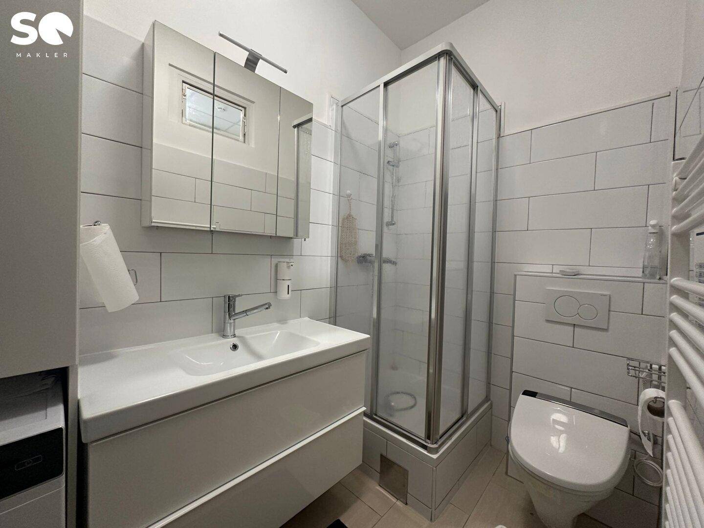 Helles Badezimmer mit Duschkabine, modernem Waschtisch und weiß gefliesten Wänden.