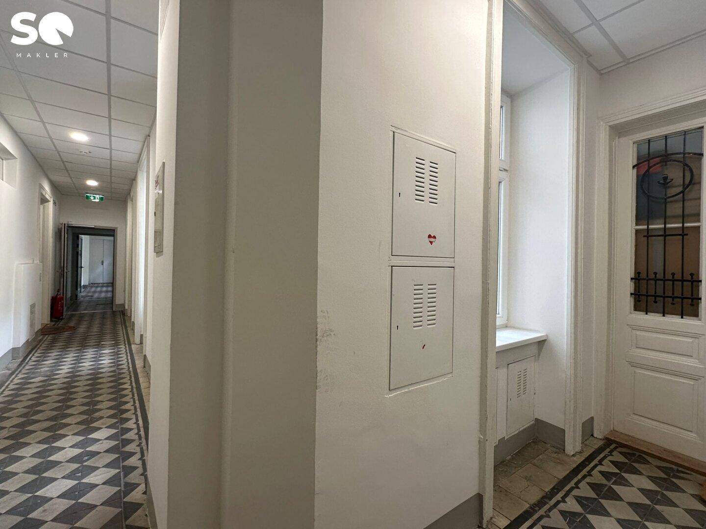 Langer Flur mit charakteristischem schwarz-weißem Fliesenboden und einer Tür mit Buntglas.