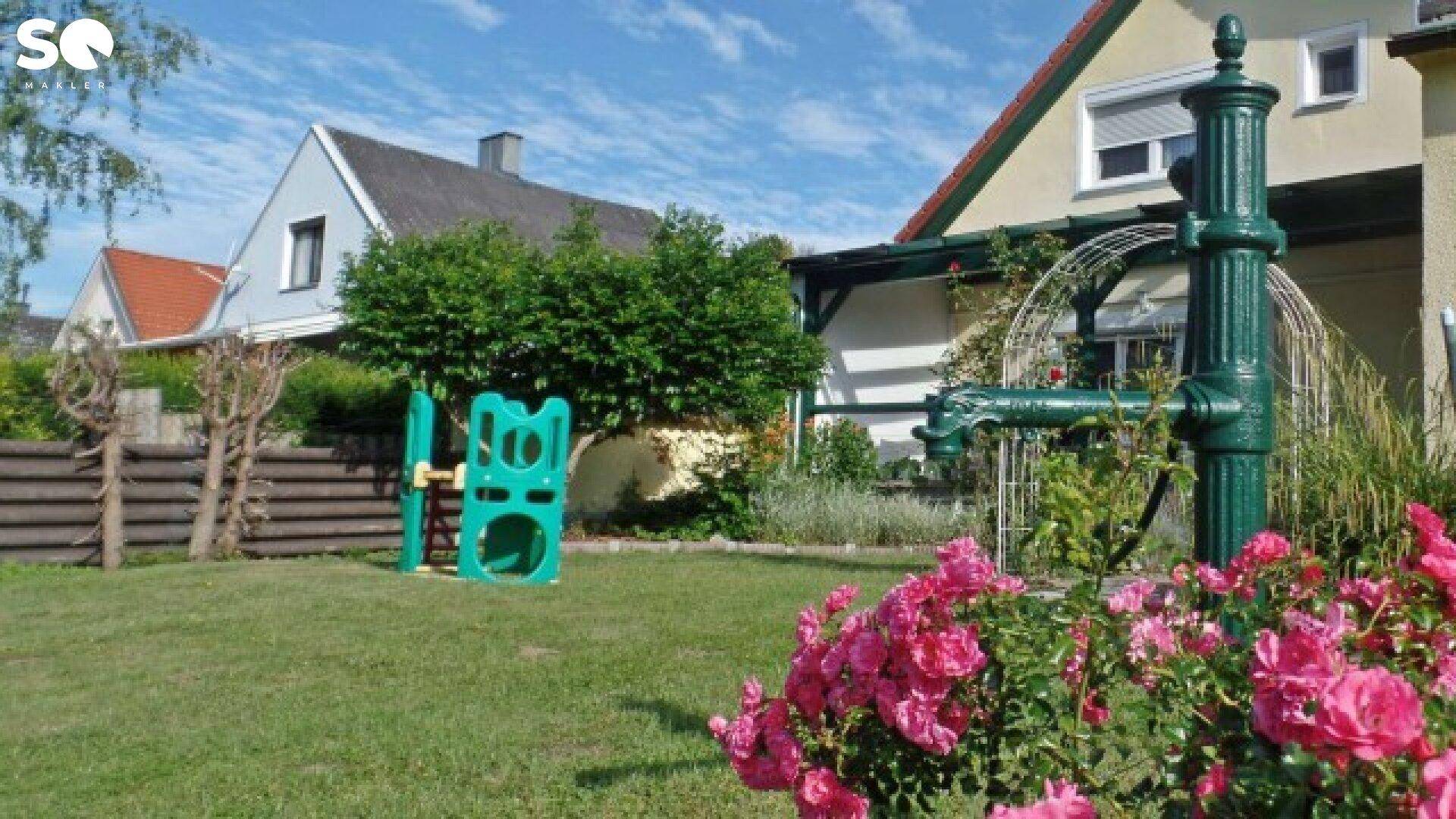 Kinderspielplatz und nostalgische Wasserpumpe im grünen Garten.