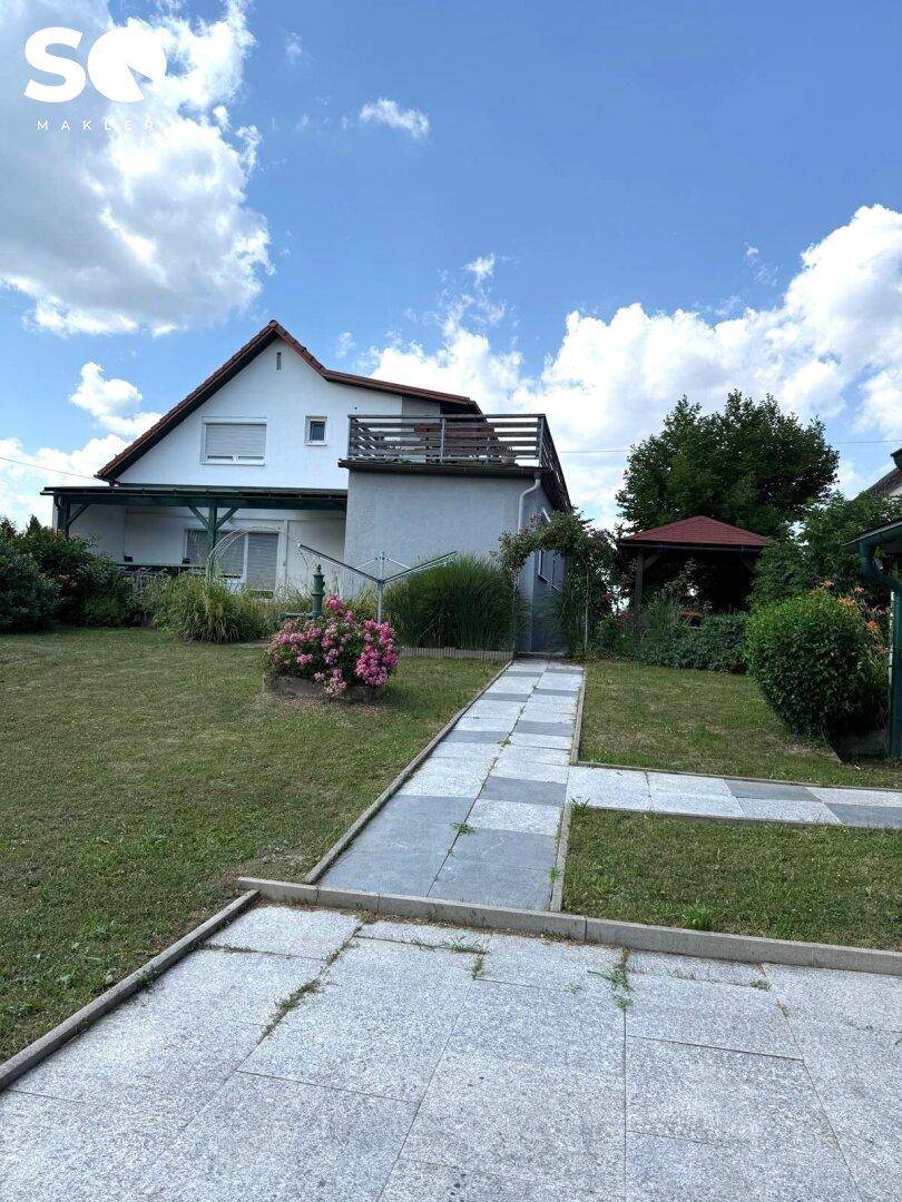 Gepflegter Garten mit Rasenfläche, gepflastertem Weg und Gartenlaube im Hintergrund.