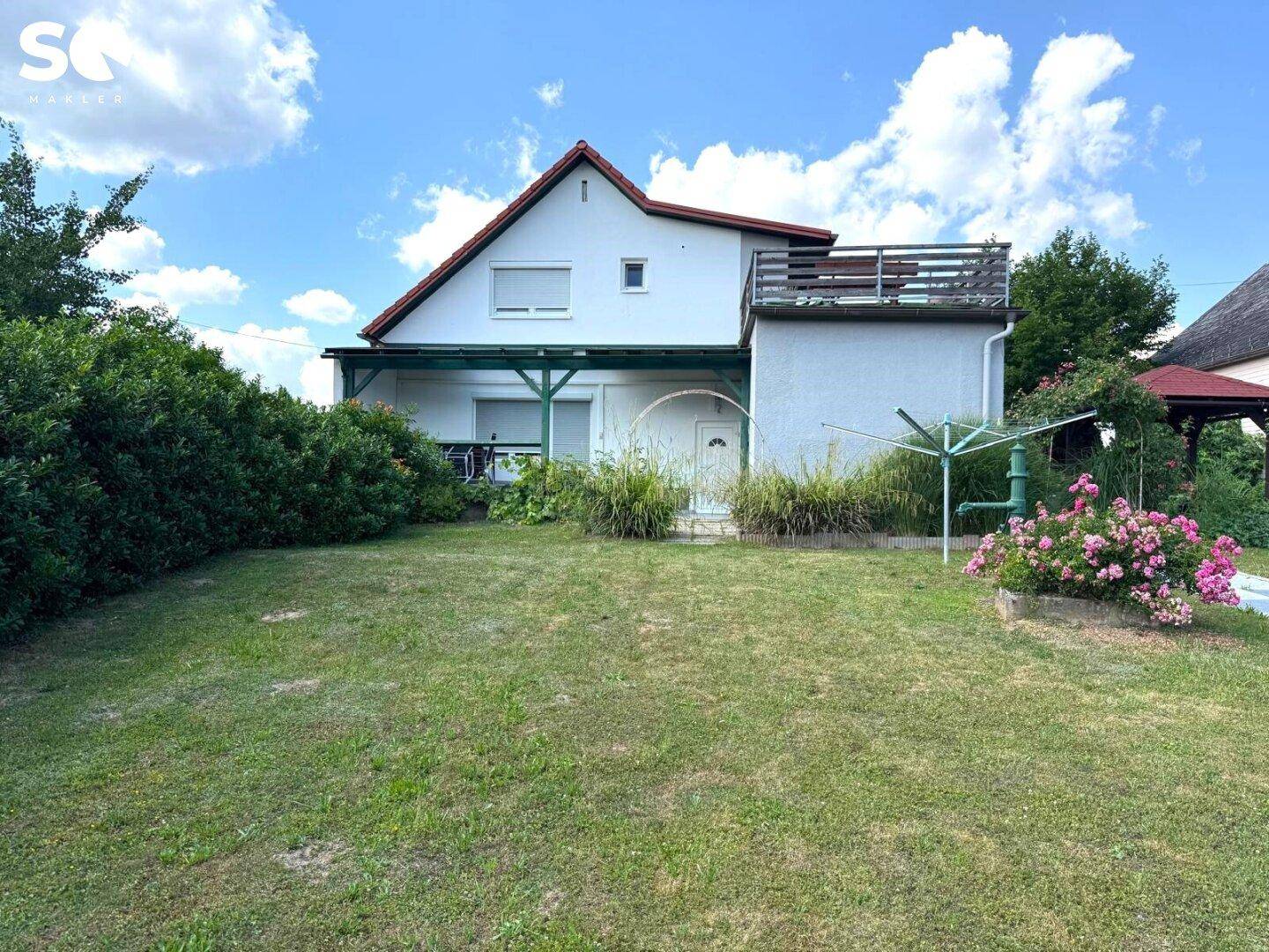Hinterer Gartenbereich mit Rasen, Wäschespinne und blühenden Sträuchern.