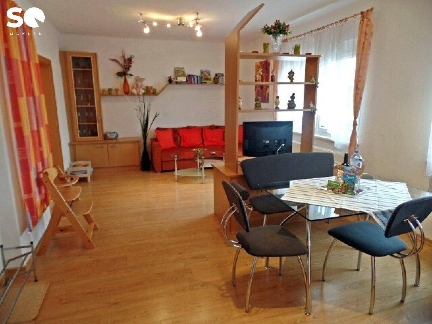 Heller Wohn- und Essbereich mit Laminatboden, rotem Sofa und Esstisch.