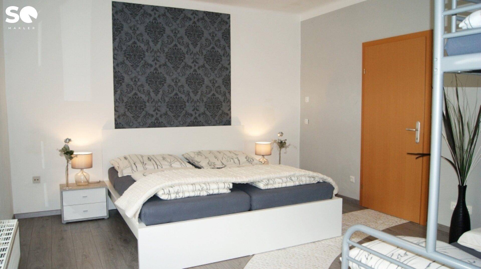 Schlafzimmer mit Doppelbett, modernem Dekor und Etagenbett im Hintergrund.