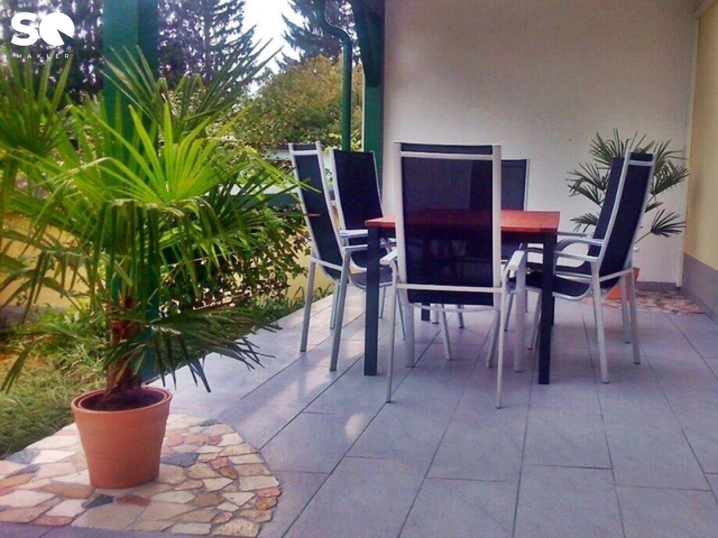 Überdachte Terrasse mit Gartenmöbeln und Topfpflanzen.
