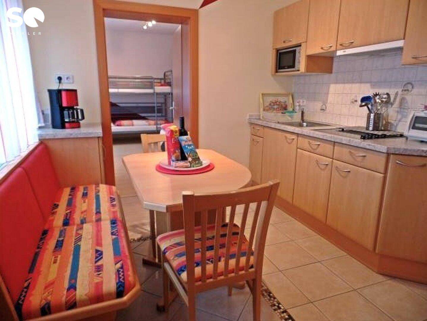 Gemütliche Küche mit Essecke, Fliesenboden und Blick in ein weiteres Schlafzimmer.