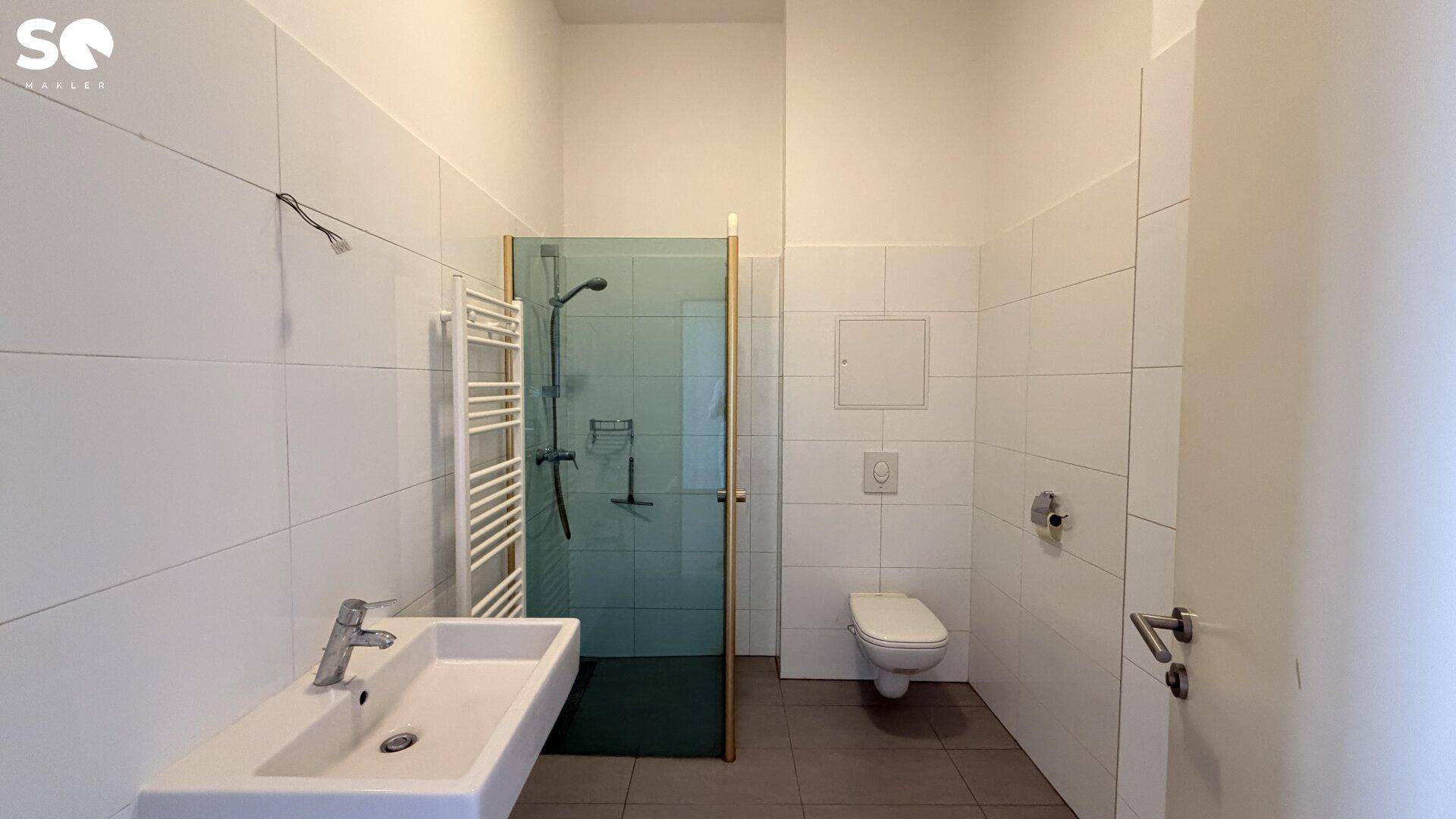 Modernes Badezimmer mit Dusche, WC, Waschbecken und beheiztem Handtuchhalter in hellen Fliesen.