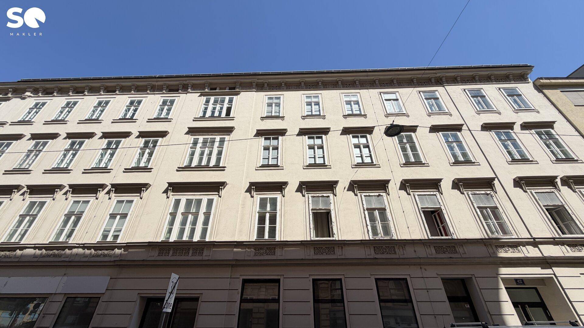 Klassische Fassade eines Mehrfamilienhauses mit vielen Fenstern unter blauem Himmel.