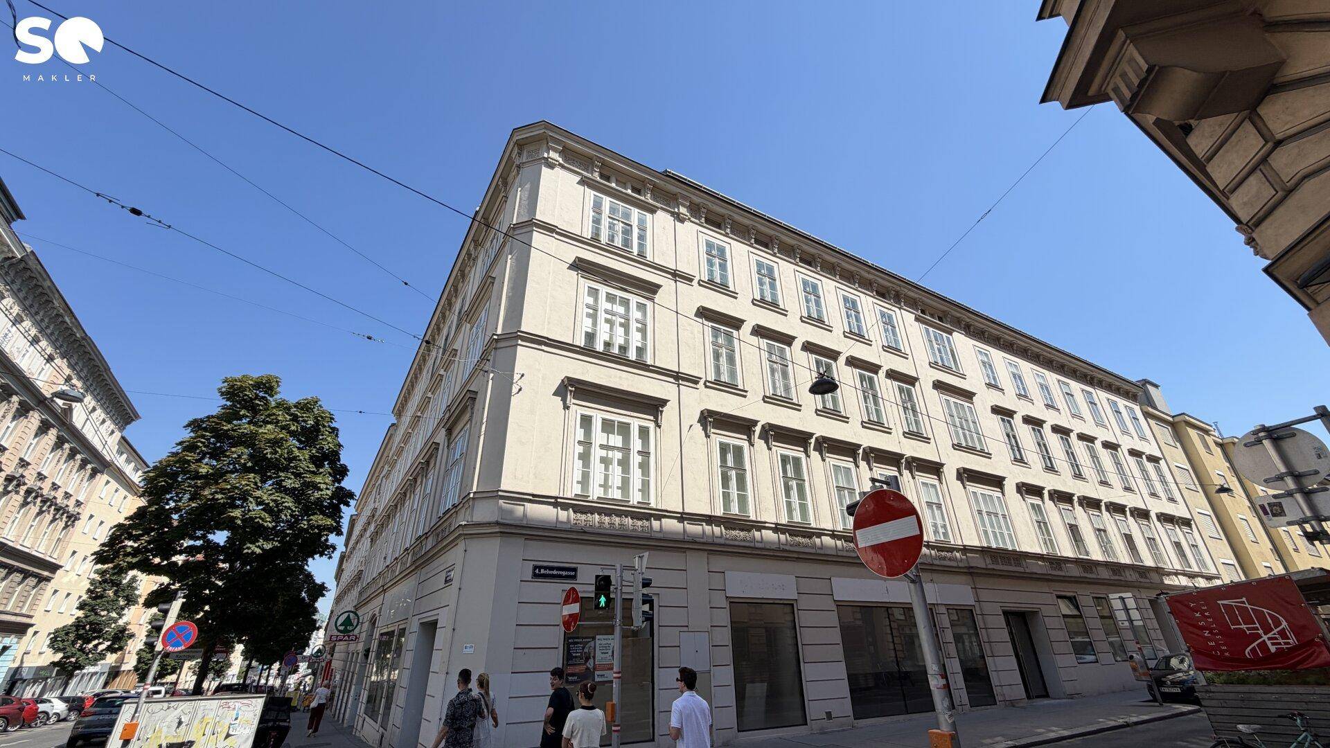 Historisches Eckgebäude mit klassischer Fassade und vielen Fenstern unter blauem Himmel.