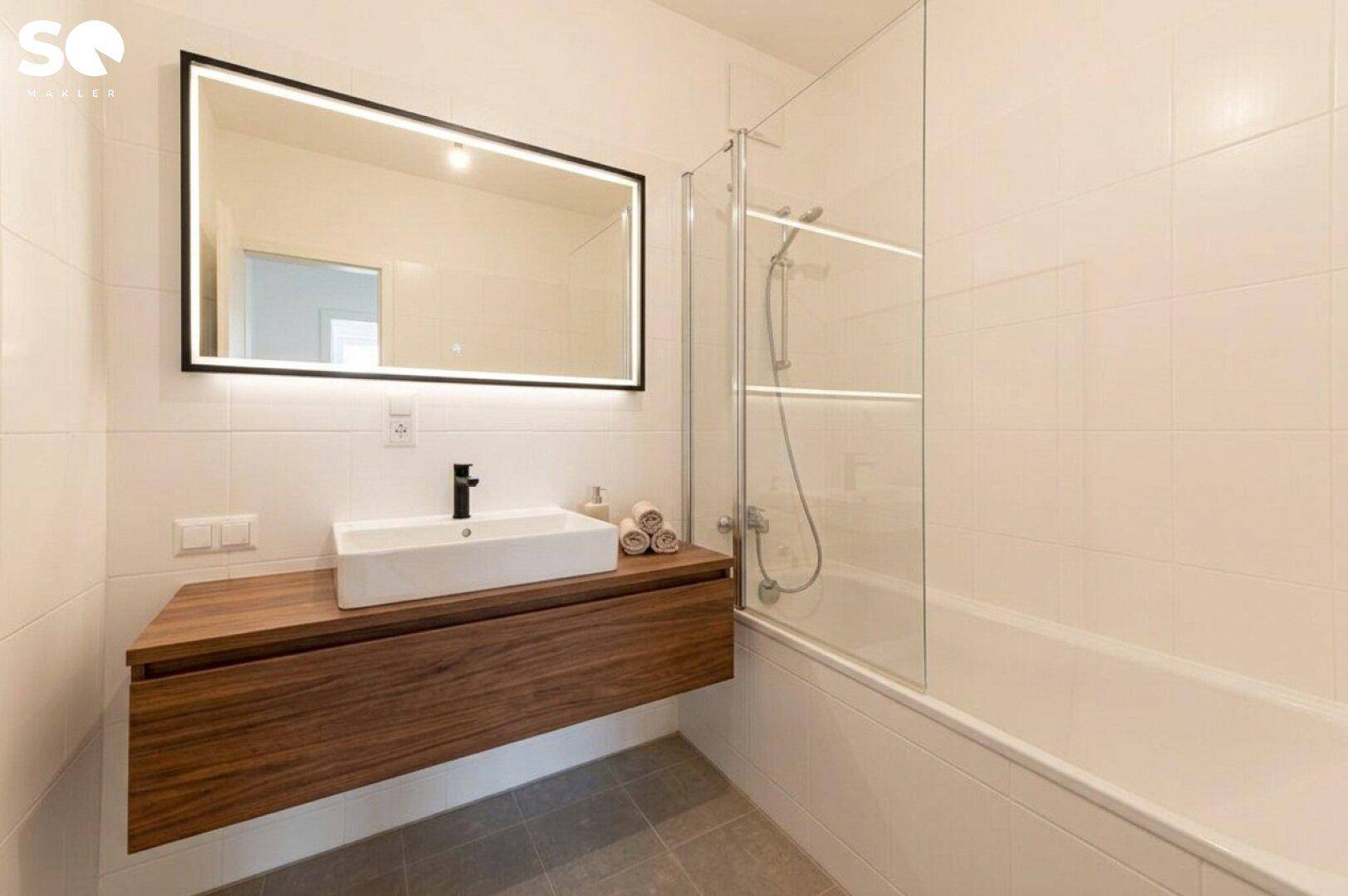 Modernes Badezimmer mit Badewanne, Holzwaschtisch und beleuchtetem Spiegel in zeitgemäßem Design.